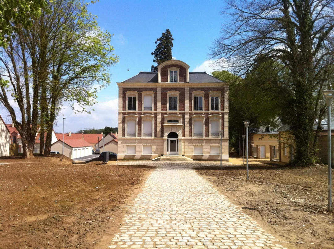 Maison ancienne avec allée pavée, entourée d'arbres.