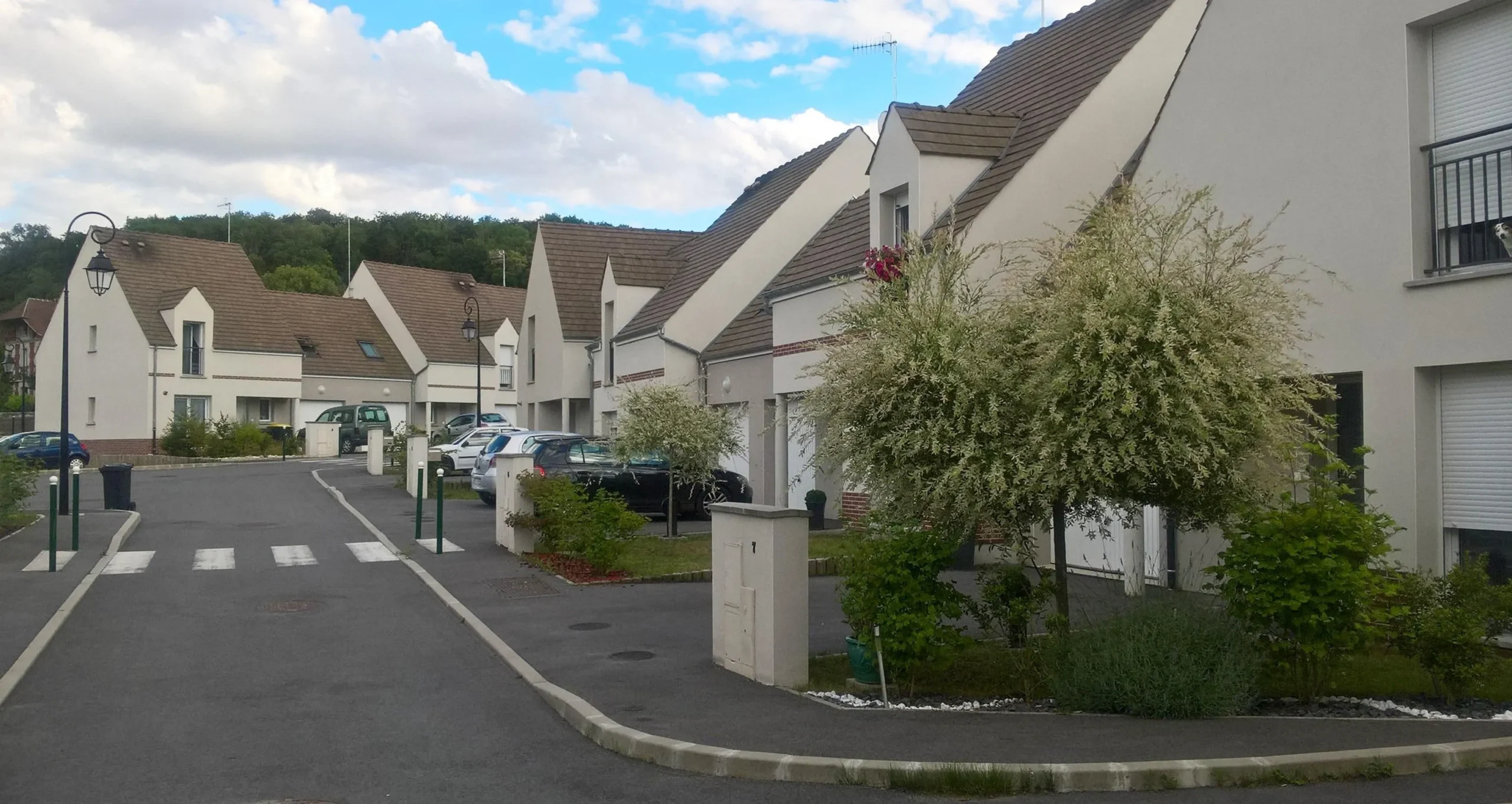 Lotissement moderne avec maisons blanches et voitures garées.